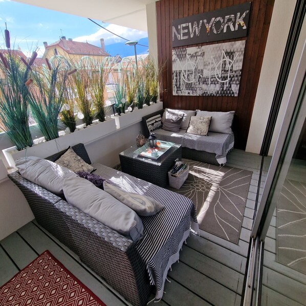 A modern outdoor seating area with a sofa and a coffee table, a decorative wall with a 'NEW YORK' sign, and a view of buildings in the background.