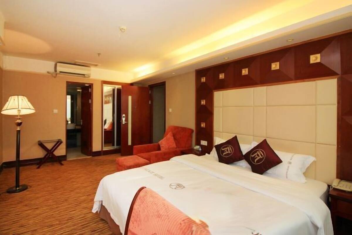 Una habitación de hotel con una cama grande, un sillón rojo, una lámpara de pie y un espejo.