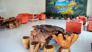 Un hall d’entrée avec des canapés rouges, une grande table basse en bois et une fresque représentant un paysage côtier.