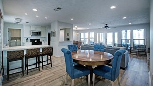 A spacious living area with a wooden dining table, blue upholstered chairs, and a gray sofa.