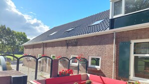 A brick house with a tiled roof, red outdoor seating, and potted plants. - De Mast bij Fort Vechten,house in old farmhouse, on the countryside near Utrecht (Bunnik)