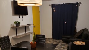 A dining area with a black table and chairs, a hanging light fixture, a potted plant, and a television on the wall. - Casa Raquelina (Ensenada)
