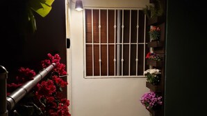 A narrow entrance with a metal gate, a window with vertical bars, and potted plants on the right. - Casa Raquelina (Ensenada)