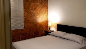 A bedroom with a bed, a nightstand with a lamp, a ceiling fan, and a window with blinds. - Casa Raquelina (Ensenada)