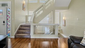 Un vaste salon doté d’un plancher en bois, d’un escalier avec des rampes en verre et offrant une vue sur l’extérieur grâce à de grandes fenêtres.