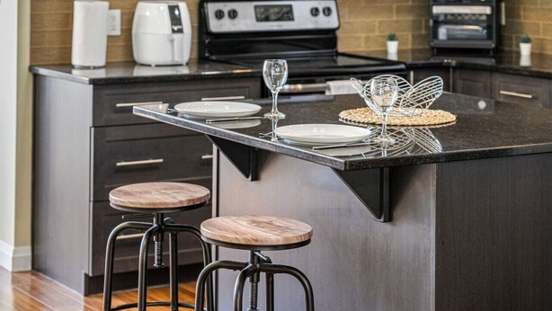 Une cuisine moderne dotée d’un îlot central, d’appareils électroménagers en acier inoxydable et de tabourets en bois.