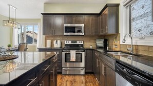 Une cuisine moderne avec des meubles en bois foncé, des appareils en acier inoxydable et un grand îlot central doté d’un plan de travail en verre.
