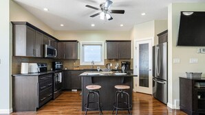 Une cuisine moderne avec des meubles de couleur sombre, des appareils en acier inoxydable, un îlot central doté de tabourets et un ventilateur de plafond.
