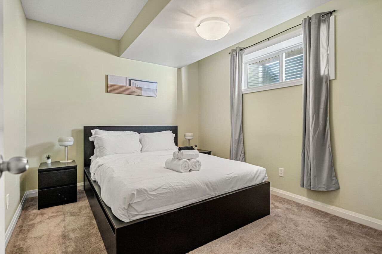 A bedroom with a bed, nightstands, a wall-mounted lamp, a window with curtains, and a ceiling light.