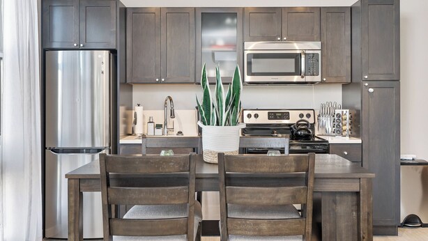 A modern kitchen with dark wood cabinets, stainless steel appliances, a central island with chairs, and a potted plant. - Beautiful 1-Bedroom Apartment@Walk to Uptown@Fast WiFi@In-Unit W/D (Minneapolis)