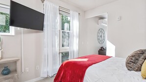 A bedroom with a bed, a TV mounted on the wall, a window with curtains, a clock, and a small table with a vase. - Beautiful 1-Bedroom Apartment@Walk to Uptown@Fast WiFi@In-Unit W/D (Minneapolis)