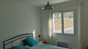 A bedroom with a bed, a nightstand, a lamp, a window, and a view of the outside. - Maison de Vacances Plain Pied 6 Couchages -2 sdb - Jardin -vernet les Bains (Vernet-les-Bains)
