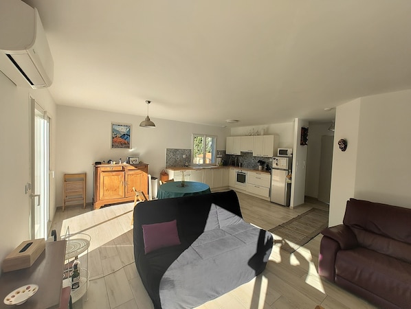 A spacious living area with a sofa, a dining table, and a kitchen in the background. - Maison de Vacances Plain Pied 6 Couchages -2 sdb - Jardin -vernet les Bains (Vernet-les-Bains)