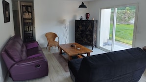 A living room with a purple sofa, a black sofa, a wooden coffee table, a wicker chair, a bookshelf, and a cabinet with a decorative tree design. - Maison de Vacances Plain Pied 6 Couchages -2 sdb - Jardin -vernet les Bains (Vernet-les-Bains)