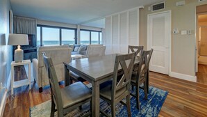 Una sala de estar moderna con comedor, ventanas amplias, ventilador de techo y vista al océano.