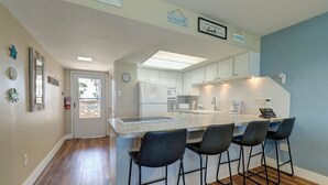 Una cocina moderna con una isla central, taburetes de bar y vistas al exterior.