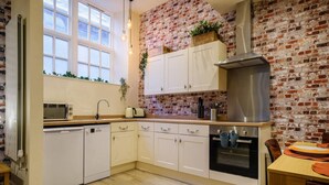 Una cocina con armarios blancos, pared de ladrillo, campana de acero inoxidable y ventana con persianas.