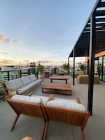 Terraço no telhado com móveis de exterior, incluindo sofás e uma mesa de centro, e vista para a paisagem urbana.
