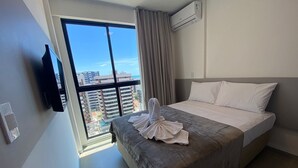 A hotel room with a large window, a bed with a grey bedspread, white pillows, and a towel on the bed. - Edificio Liv P.Verde Apto 1108 (Maceió)