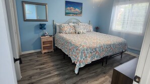 A bedroom with a bed, a nightstand, a ceiling fan, a window with blinds, and a door. - Cozy Pool side Condo, 5 min from the beach! (Little River)