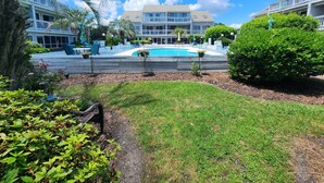 A pool area with a wooden deck, lounge chairs, and a building with multiple balconies in the background. - Cozy Pool side Condo, 5 min from the beach! (Little River)