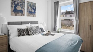 A bedroom with a large bed, two wall-mounted paintings, a window with curtains, a bedside table with a lamp, and a wooden wardrobe. - Gloster Town House Gorgeous Family Home Barnstaple (Barnstaple)