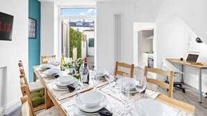 A modern dining area with a long table set for six, white walls, and a view of the garden and street outside. - Gloster Town House Gorgeous Family Home Barnstaple (Barnstaple)