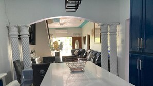 A kitchen with a white countertop, dark cabinets, and a dining area with a table and chairs. - 1 Bedroom Blissful Retreat - A/C & Private Garden (Gravel Hill District)