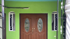 A green-walled entrance with a brown double door featuring glass panels, a metal gate, and a black doormat. - 1 Bedroom Blissful Retreat - A/C & Private Garden (Gravel Hill District)