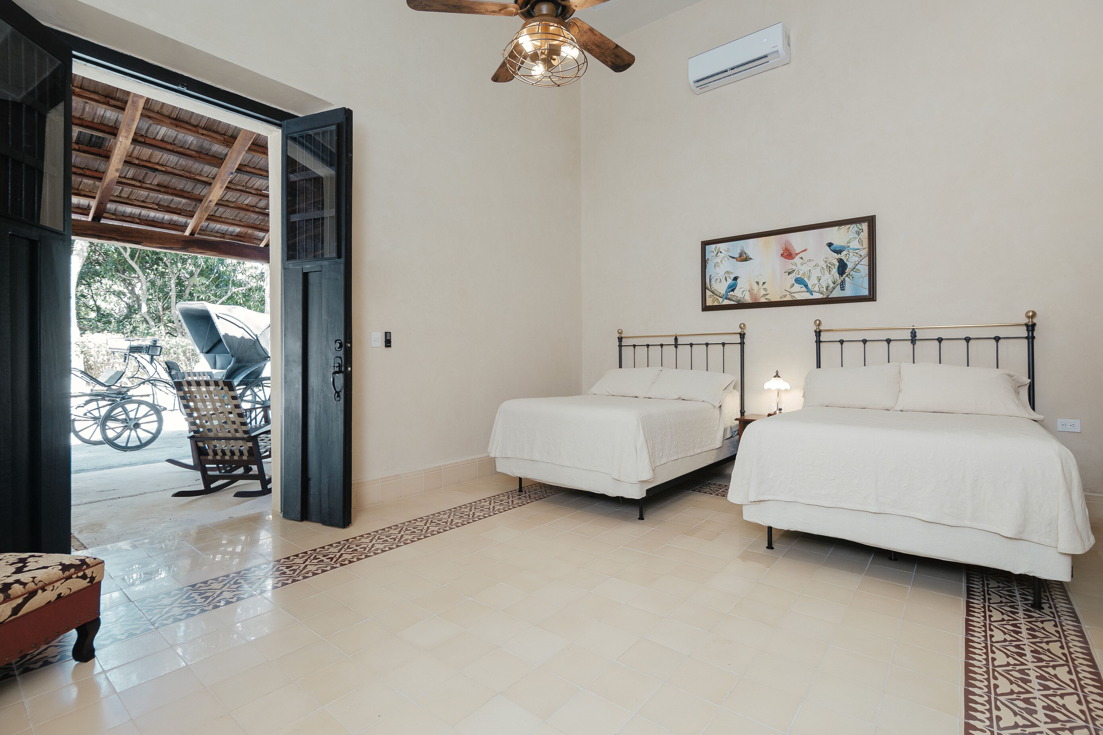 A bedroom with two beds, a ceiling fan, a painting, and a bicycle outside.
