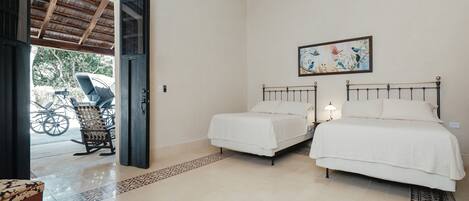 A bedroom with two beds, a ceiling fan, a painting, and a bicycle outside.