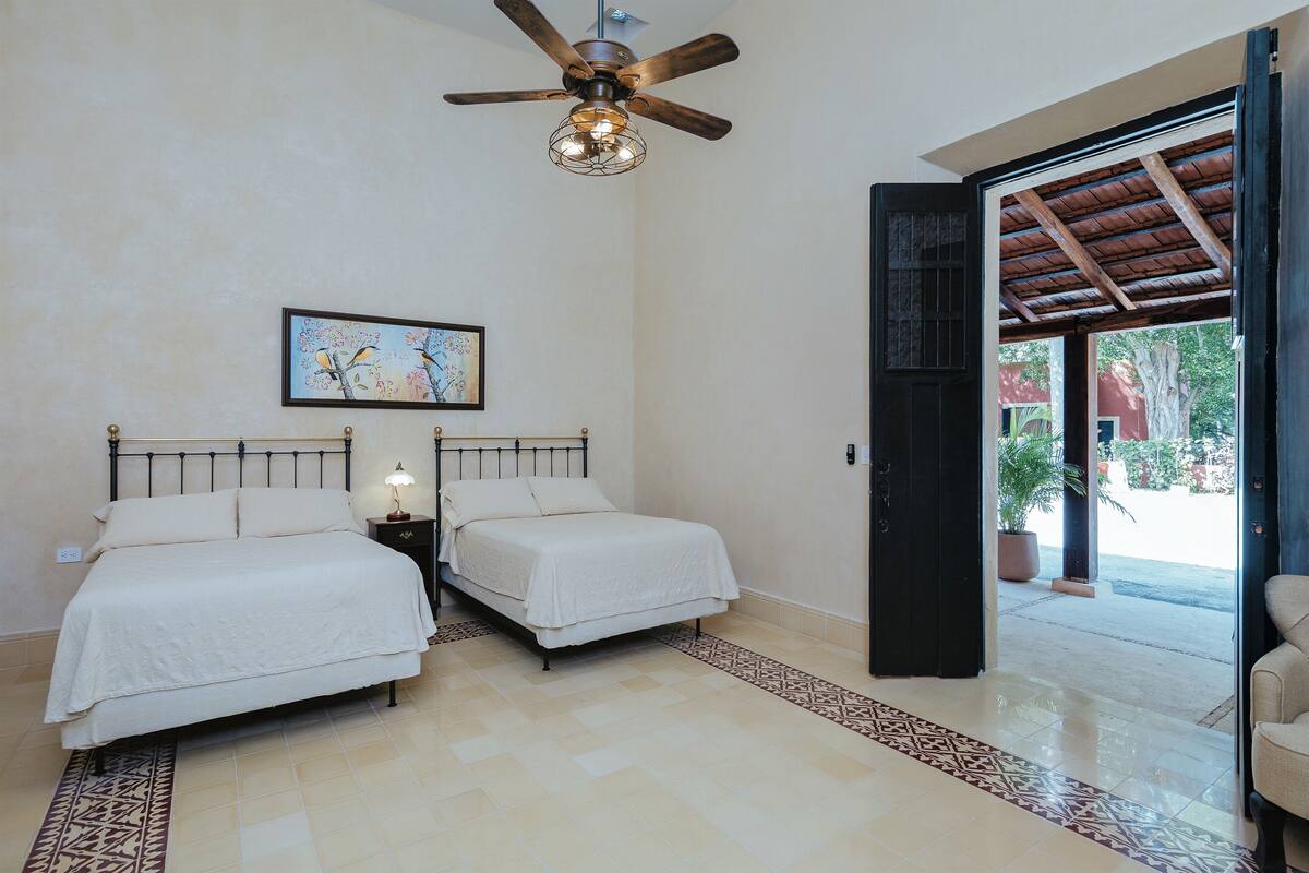 A bedroom with two beds, a ceiling fan, a nightstand with a lamp, and a patterned rug.