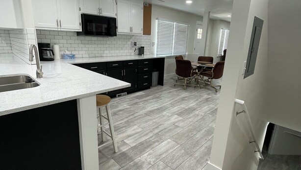 A modern kitchen with white cabinets, a black microwave, and a grey tiled backsplash. - Center of town, newly renovated home, lots of parking and space for family (Cedar City)