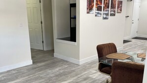 A modern interior with a herringbone-patterned wooden floor, a glass-top table, brown upholstered chairs, and a white wall with framed artwork. - Center of town, newly renovated home, lots of parking and space for family (Cedar City)