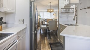 A modern kitchen with white cabinetry, stainless steel appliances, and a dining area with a chandelier. - Loggerhead 282- Coastal Chic Gulf Front (Sanibel)