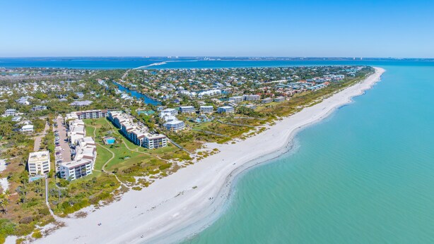 An aerial view of a coastal resort with beachfront properties, a marina, and a long sandy beach. - Loggerhead 282- Coastal Chic Gulf Front (Sanibel)