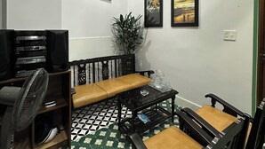 A living room with a sofa, coffee table, and chairs, a television, and framed pictures on the wall. - Nineties Homestay  (Hue)