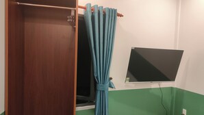 A room with a wooden wardrobe, a blue curtain, a blackboard, and a small wooden table with a power outlet. - Nineties Homestay  (Hue)