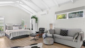 Ein modernes Schlafzimmer mit einem Bett, einem grauen Sofa, einem Sessel und einem kleinen Tisch.