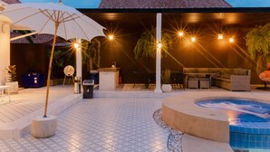 Un espace extérieur bien éclairé, avec une terrasse, un jacuzzi, des sièges et des parasols.