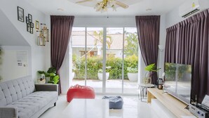 Un salon moderne avec un canapé gris, un fauteuil poire rouge, une table basse en bois et un téléviseur posé sur un meuble en bois.