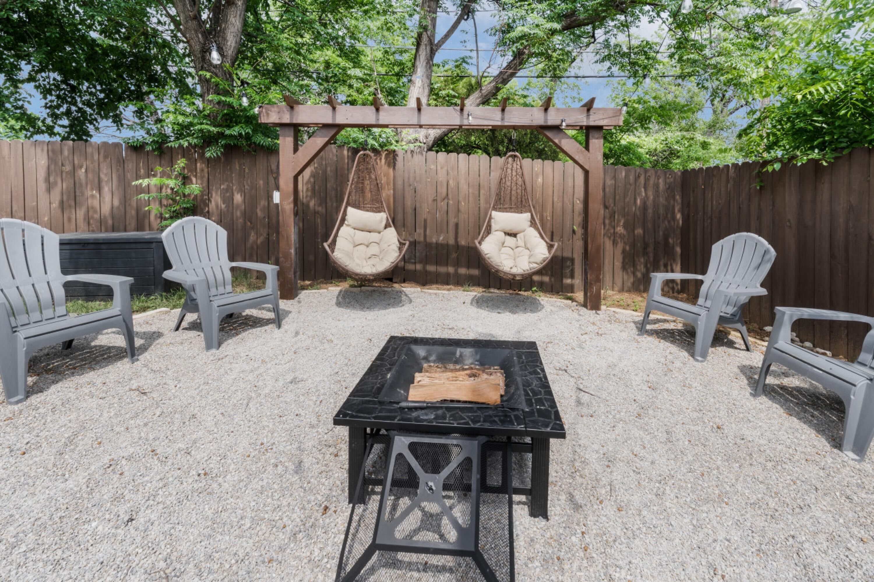 An outdoor patio with a black grill table, two Adirondack chairs, and two hanging egg chairs.