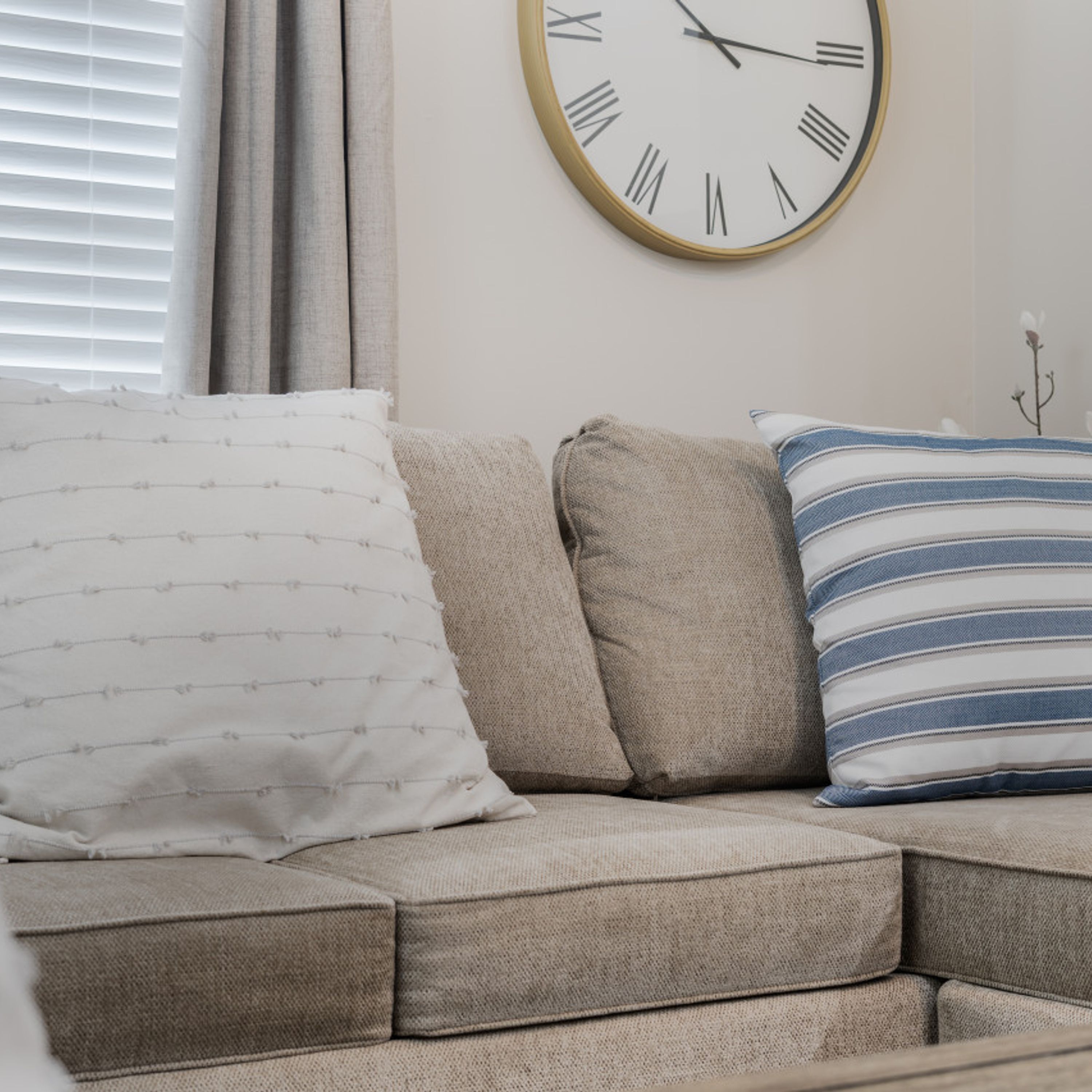 A sectional sofa with two pillows, one striped and one with a pattern, against a plain wall with a round wall clock.