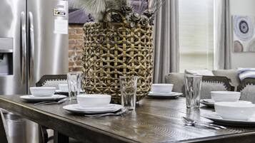 A dining table set with white plates, bowls, and clear glasses, with a woven basket containing dried flowers in the center.