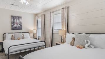 A hotel room with two beds, a ceiling fan, a painting of a bridge, and a window with curtains.