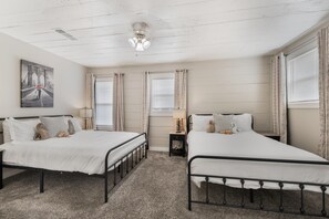 Een slaapkamer met twee bedden, een plafondventilator, een schilderij en een raam met gordijnen.