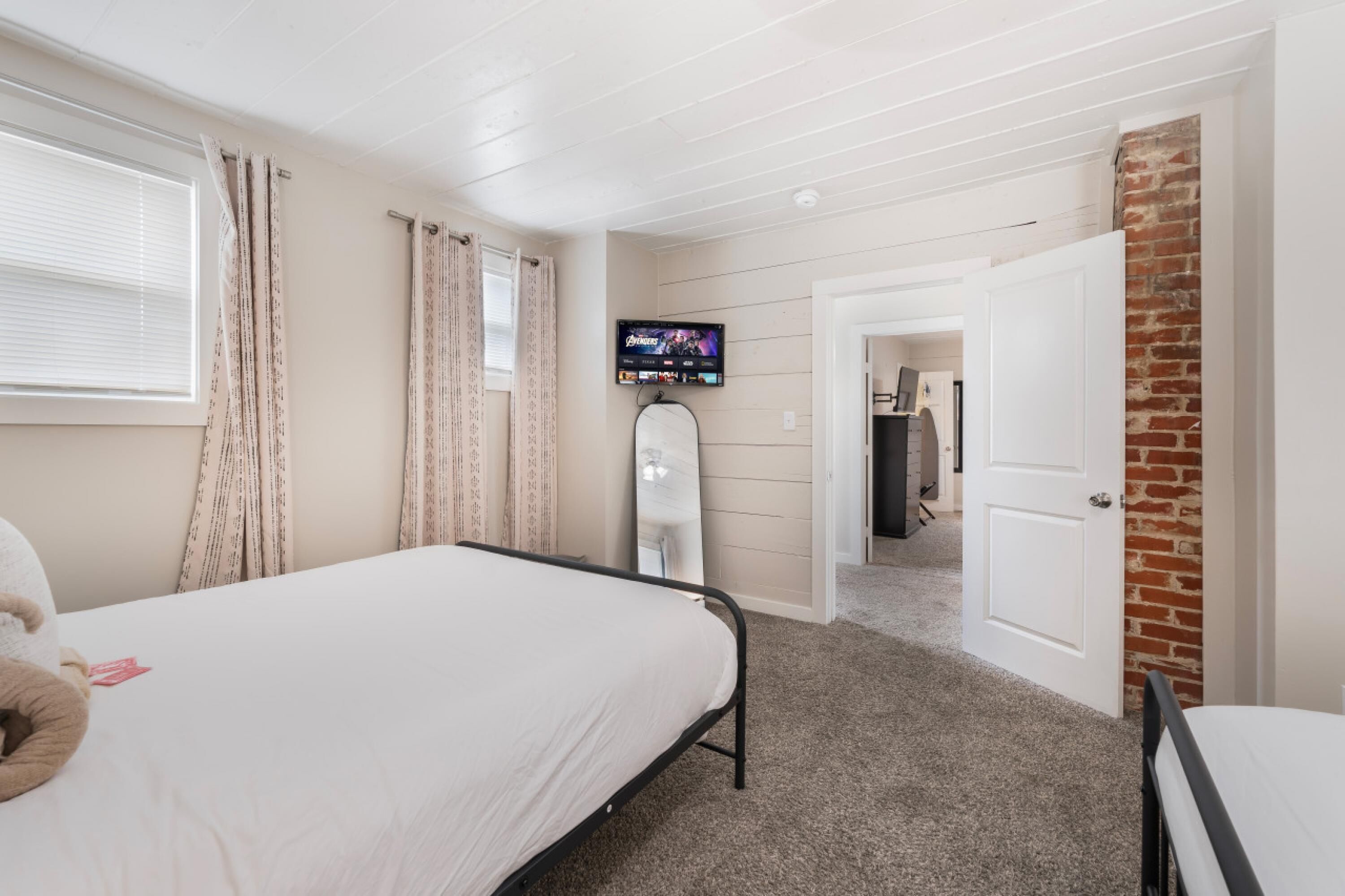 A bedroom with a bed, a TV mounted on the wall, and a door leading to another room.