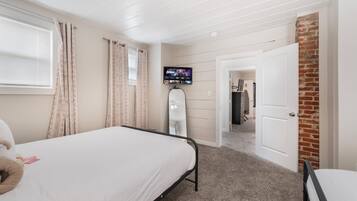 A bedroom with a bed, a TV mounted on the wall, and a door leading to another room.