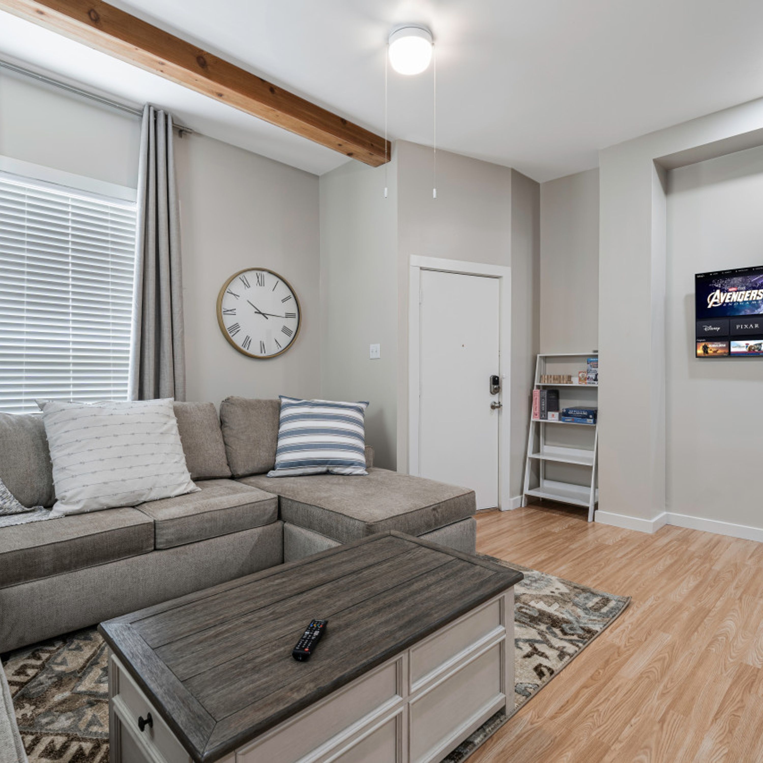 A living room with a sectional sofa, a coffee table, a clock, a television, and a door.