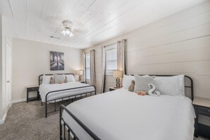 Een hotelkamer met twee enkele bedden, een plafondventilator, een schilderij aan de muur en een raam met gordijnen.